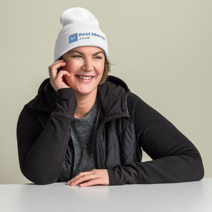 White Cuffed Best Merch Beanie with blue logo, worn by smiling woman in black vest. Comfortable and stylish branded merch.